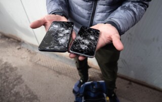 Ein Geflüchteter hält seine beiden von der Polizei zerstörten Handys in den Händen.