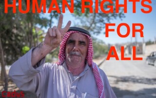 Ein Mann in Kobané mit traditioneller Kopfbedeckung lächelt und zeigt ein Peace-Zeichen. Dazu der Spruch: "Human Rights for all"