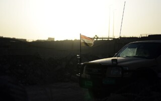 The sun rises behind a SUV with an Iraqi flag atached to it.